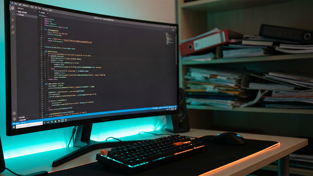 Pantalla de ordenador mostrando código Python para automatizar tareas de oficina con fondo de papeles desordenados.